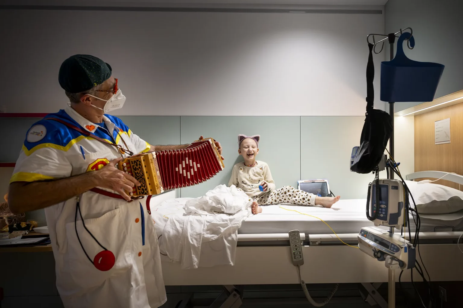Un Doctor Sonrisa toca el acordeón junto a la cama de una niña hospitalizada que se ríe