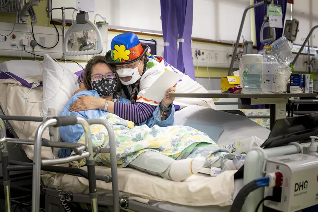 Doctor Sonrisa de la Fundación Theodora con mascarilla juega con una niña tumbada en su cama