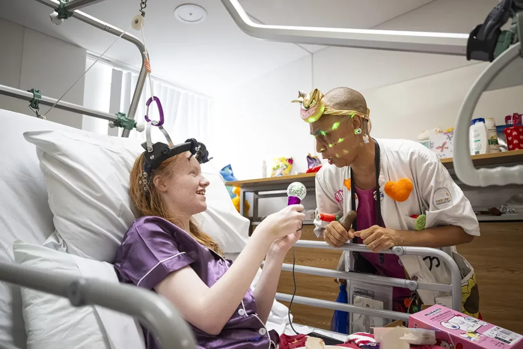 Doctora Sonrisa de la Fundación Theodora ríe con una paciente sentada en su cama