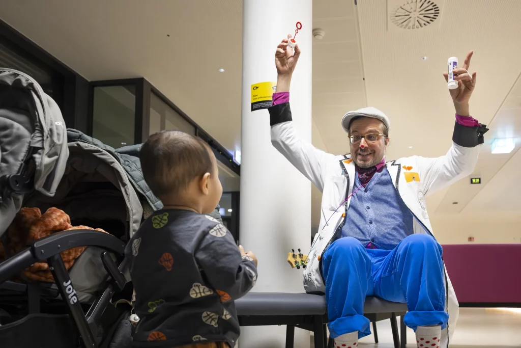 Un Doctor Sonrisa de la Fundación Theodora levanta los brazos de alegría delante de un niño en el hospital