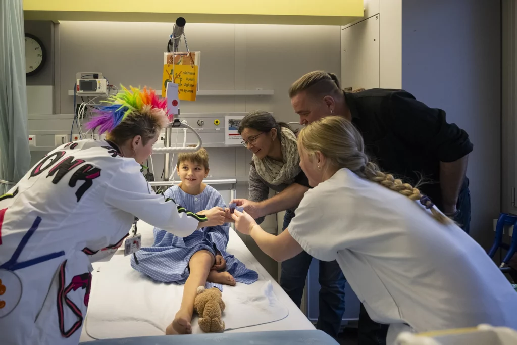 Doctor Sonrisa de la Fundación Theodora entretiene a un niño en camilla rodeado de su familia
