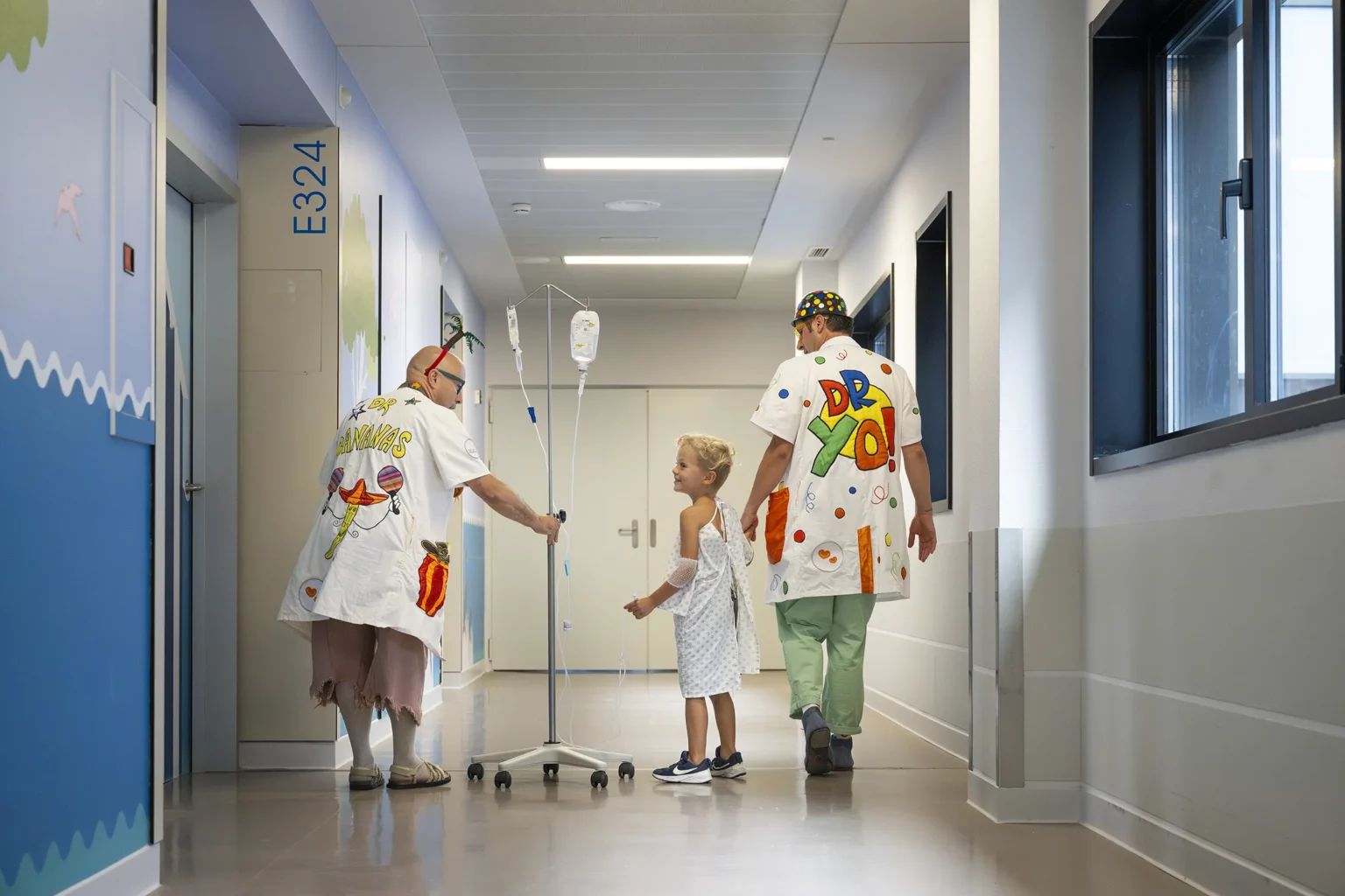 Dos Doctores Sonrisa de la Fundación Theodora acompañan a un niño con su gotero por el pasillo del hospital