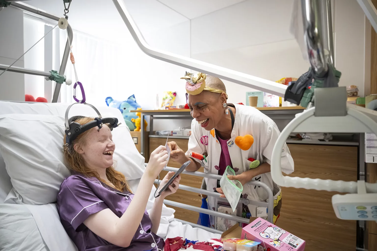 Una niña ingresada se ríe en su cama de hospital con un Doctor Sonrisa de la Fundación Theodora
