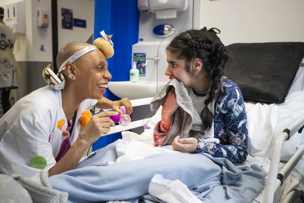 Doctora Sonrisa de la Fundación Theodora juega con una chica sentada en su cama