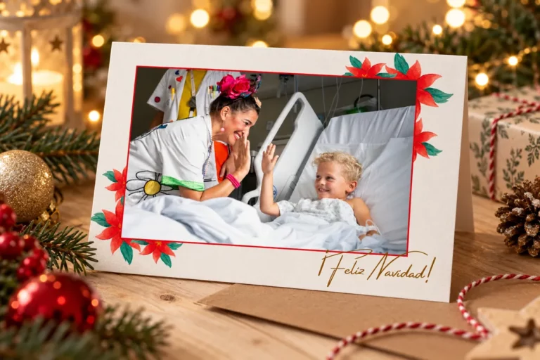 Tarjeta de Navidad solidaria con la foto de una Doctora Sonrisa chocando los cinco con un niño en su cama del hospital, con flores de Pascua y «¡Feliz Navidad!»