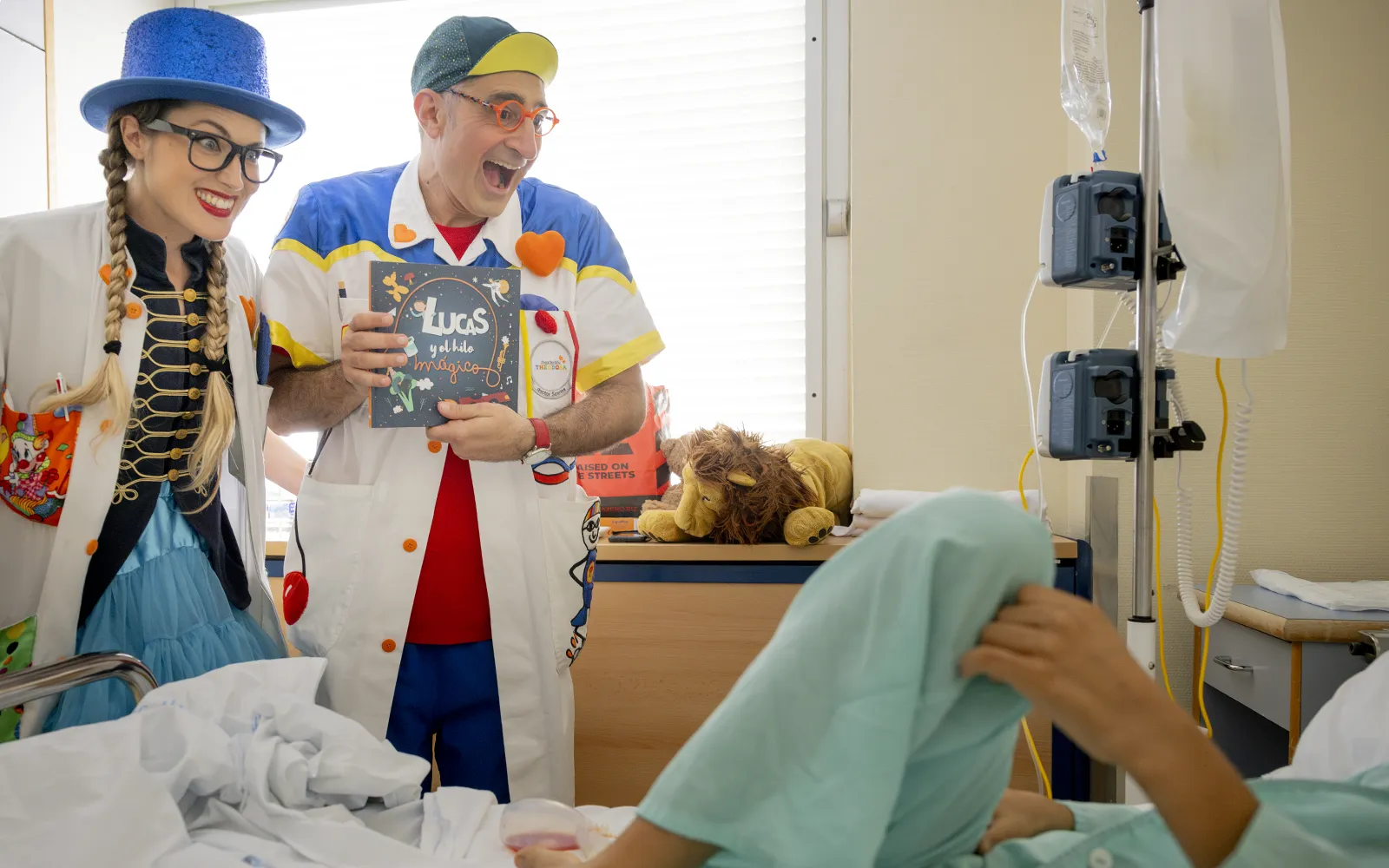 Dos Doctores Sonrisa de la Fundación Theodora entregan un libro a un niño en su habitación del hospital